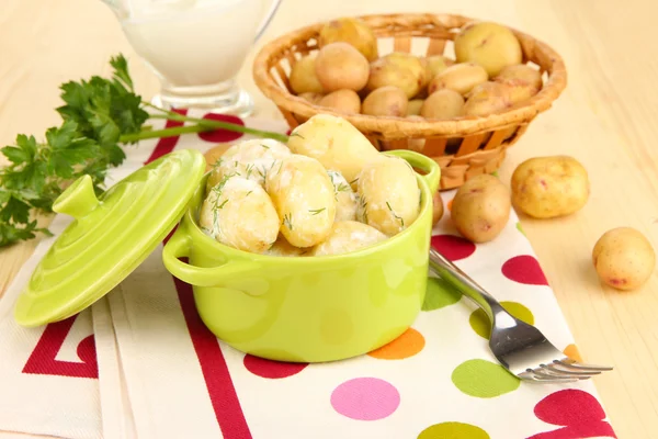 Anbudsförfarande unga potatis med gräddfil och örter i stekpanna på träbord närbild — Stockfoto