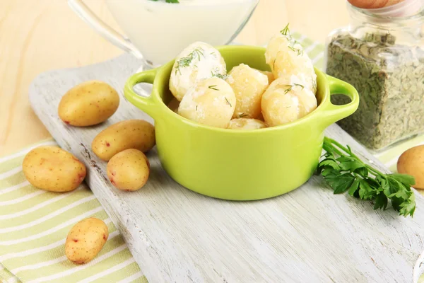 Tender young potatoes with sour cream and herbs in pan on wooden board on table close-up — Stock Photo, Image