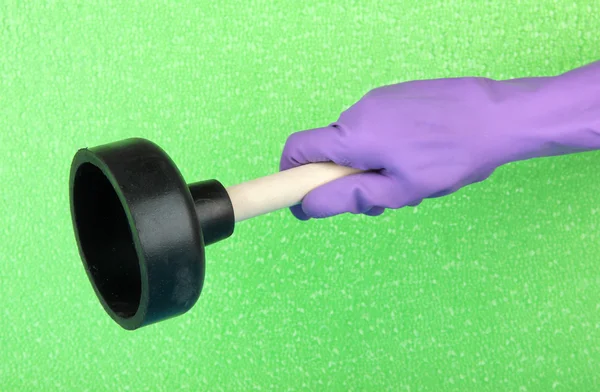 緑の背景に手で洗面所のプランジャー — ストック写真