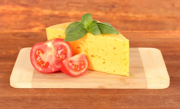 Cheese,basil and tomato on cutting board on wooden background — Stock Photo, Image