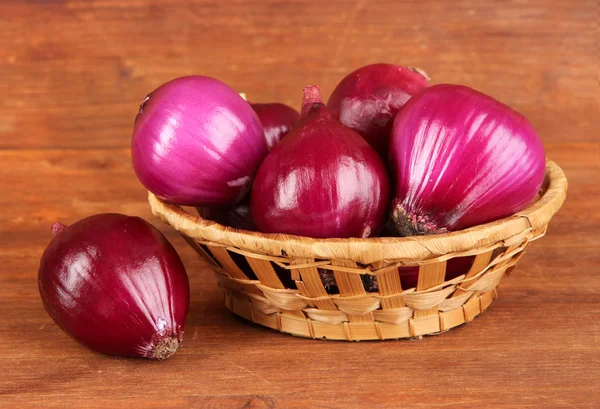 Purple onion in wicker basket on wooden background — Stock Photo, Image