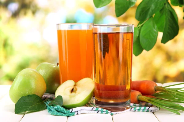 Glas juice, äpplen och morötter på vita träbord, på grön bakgrund — Stockfoto