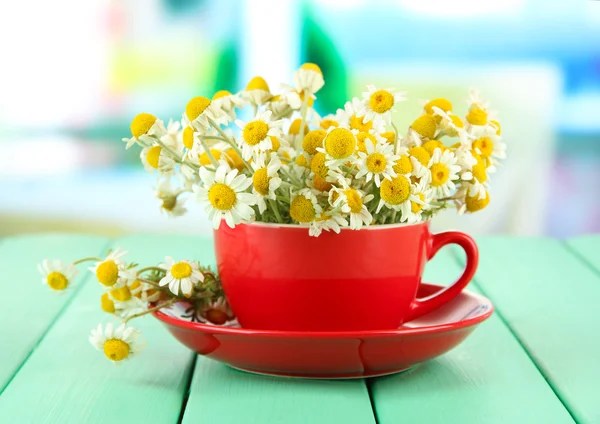 Bouquet of chamomile flowers in cup, on bright background — Stock Photo, Image