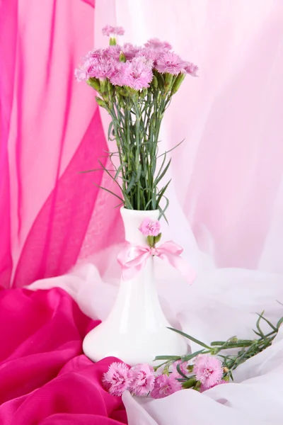 Muitos pequenos cravos cor-de-rosa em vaso no fundo de tecido leve — Fotografia de Stock