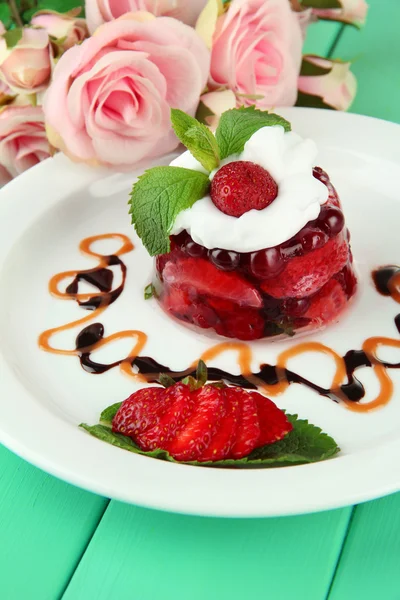 Sabroso postre de gelatina con bayas frescas, sobre fondo de rosas rosadas —  Fotos de Stock