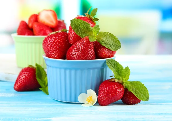 Ripe sweet strawberries in bowls on blue wooden table — Stock Photo, Image