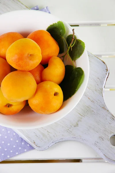 Apricots in plate on board on napkin on wooden table — Stock Photo, Image