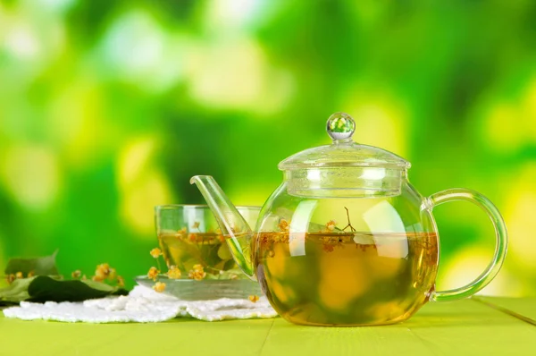 Kettle and cup of tea with linden on wooden table on nature background — Stock Photo, Image