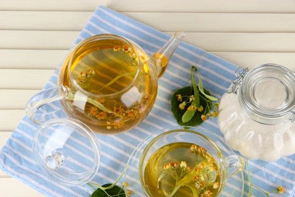 Hervidor de agua y taza de té con tilo en servilleta sobre mesa de madera —  Fotos de Stock