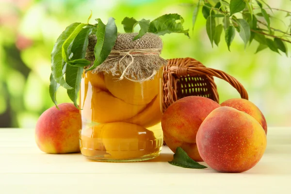 Jar of canned peaches and fresh peaches on wooden table, outside