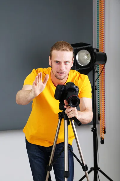 Fotógrafo bonito com câmera no trabalho, no fundo do estúdio de fotografia — Fotografia de Stock