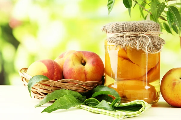 Jar of canned peaches and fresh peaches on wooden table, outside — Stock Photo, Image