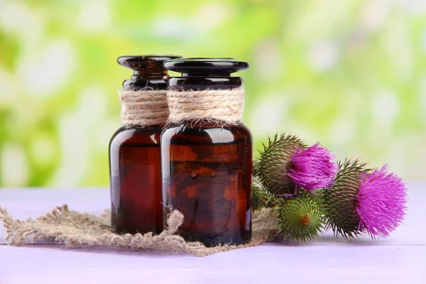 Medicine bottles with thistle flowers on nature background — Stock Photo, Image