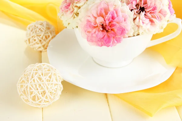 Rosen in Tasse auf Holztisch auf gelbem Stoff Hintergrund — Stockfoto
