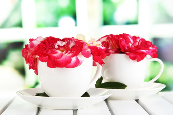 Rosen in Tassen auf dem Tisch auf Fensterhintergrund — Stockfoto