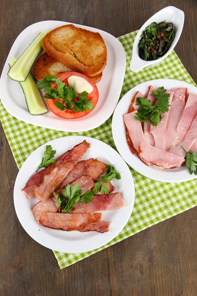 Tocino sobre platos en servilleta sobre mesa de madera — Foto de Stock