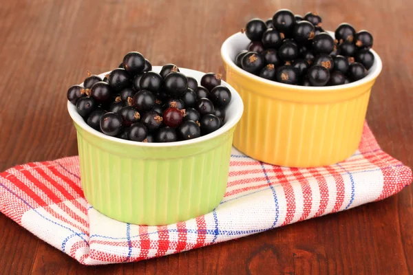 Fresh black currant in bowls on napkin on wooden background — Stock Photo, Image