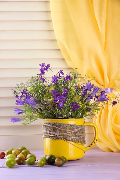 Mooi boeket van wilde bloemen in cup en bessen op houten tafel — Stockfoto