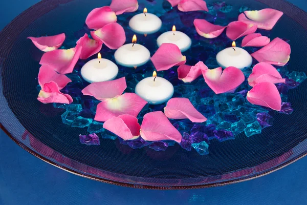 Pétalas de rosa e velas na água em vaso no fundo azul close-up — Fotografia de Stock