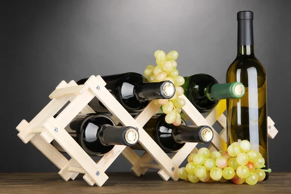 Ahşap stand gri arka plan üzerine yerleştirilen şarap şişeleri — Stok fotoğraf