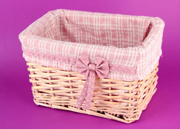 Wicket basket with pink fabric and bow, on color background — Stok fotoğraf