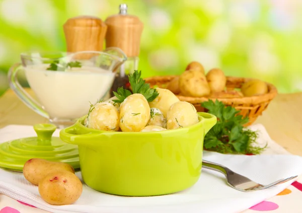 Inschrijving van jonge aardappelen met zure room en kruiden in pan op houten tafel op natuurlijke achtergrond — Stockfoto