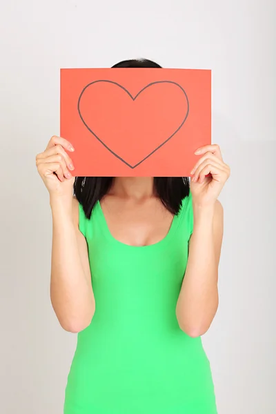 Young woman holding red painted heart on grey background — Stock fotografie