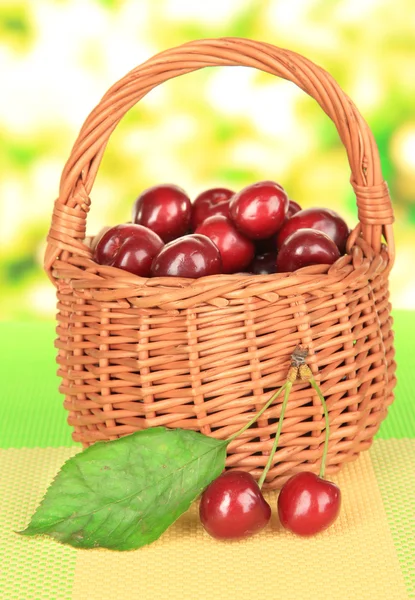 Kirschbeeren im Weidenkorb auf dem Tisch auf hellem Hintergrund — Stockfoto