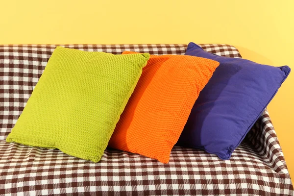 Colorful pillows on couch on yellow background — Stock Photo, Image