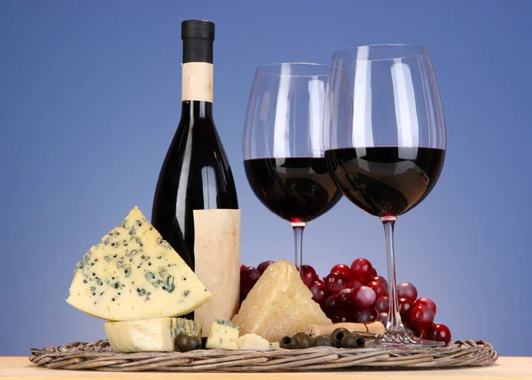 Natura morta raffinata di vino, formaggio e uva su vassoio di vimini su tavolo di legno su sfondo blu — Foto Stock