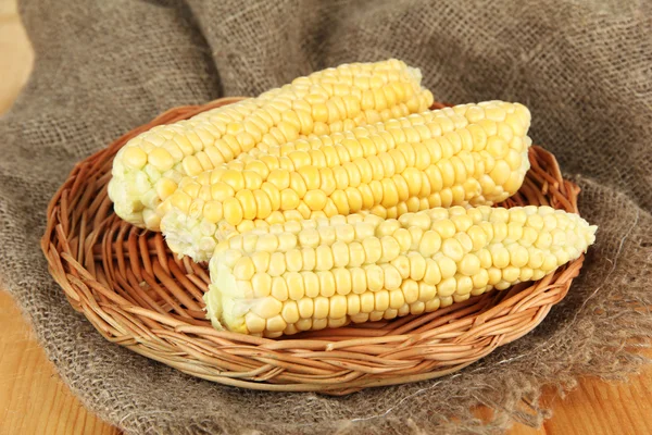 Fresh corn on wicker mat, on sackcloth background — Stock Photo, Image