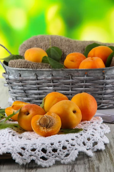 Apricots in basket on napkin on wooden table on nature background — Stock Photo, Image