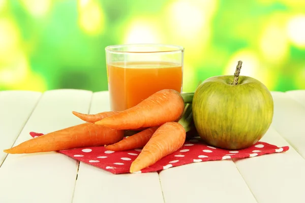 Un mucchio di carote e mela verde, vetro di succo, su tavolo di legno a colori su sfondo brillante — Foto Stock