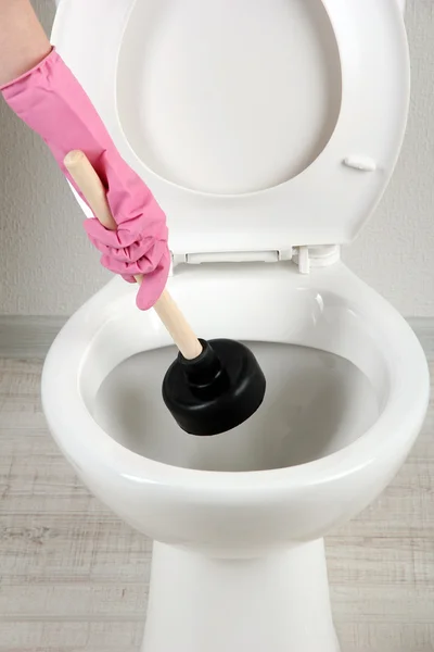 Woman uses a plunger to unclog a toilet bowl in a bathroom — Stock Photo, Image