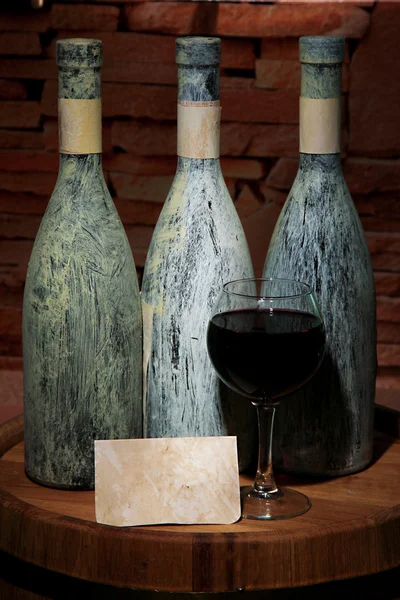 Композиция со старой бутылкой вина и бокалом вина в старом подвале, на темном фоне — стоковое фото