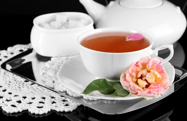 Wasserkocher und Tasse Tee aus Teerose auf metallischem Tablett auf Serviette schwarzem Hintergrund — Stockfoto