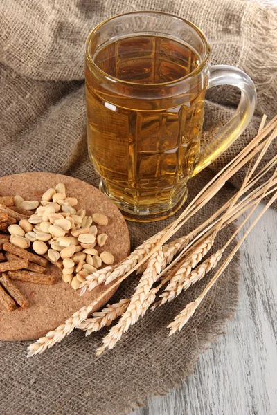 Beer in glass, crackers and nuts on bagging on wooden table — Stock Photo, Image