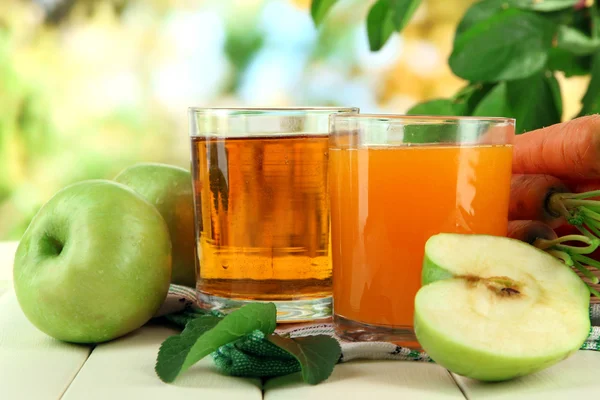 Glas juice, äpplen och morötter på vita träbord, på grön bakgrund — Stockfoto