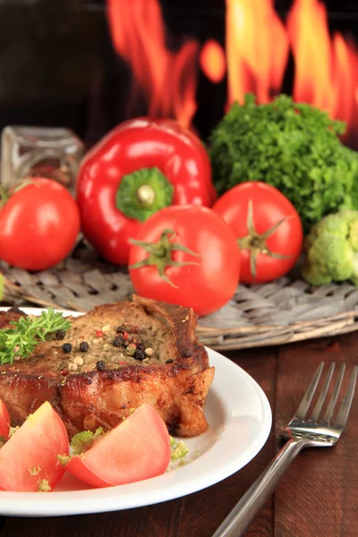 Piece of fried meat on plate on wooden table on fire background — Stock Photo, Image