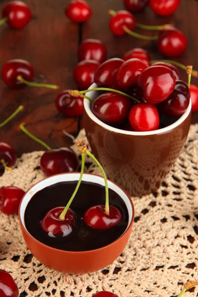 Ripe red cherry berries in cup and chocolate sauce on wooden table close-up — Stock Photo, Image