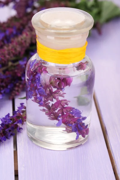 Botella de medicina con flores de salvia sobre fondo de madera morada Imagen De Stock