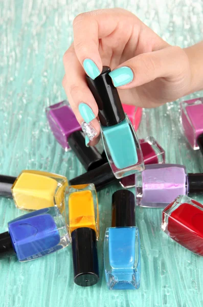 Hermosas manos de mujer con manicura azul y varias botellas con esmalte de uñas, sobre fondo de color —  Fotos de Stock