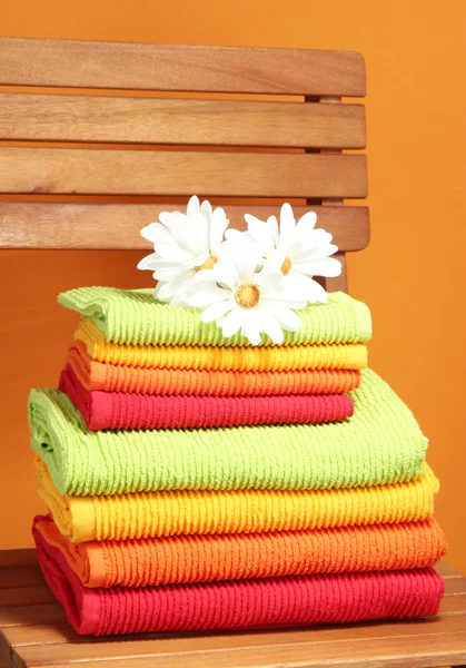 Towels and flowers on wooden chair on orange background — Stok fotoğraf