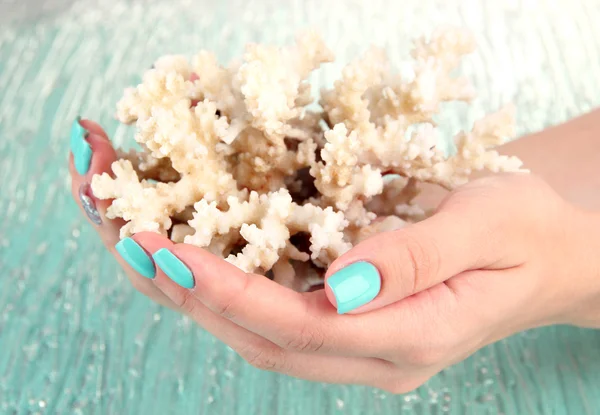 Hermosas manos de mujer con manicura azul sosteniendo coral, sobre fondo de color — Foto de Stock