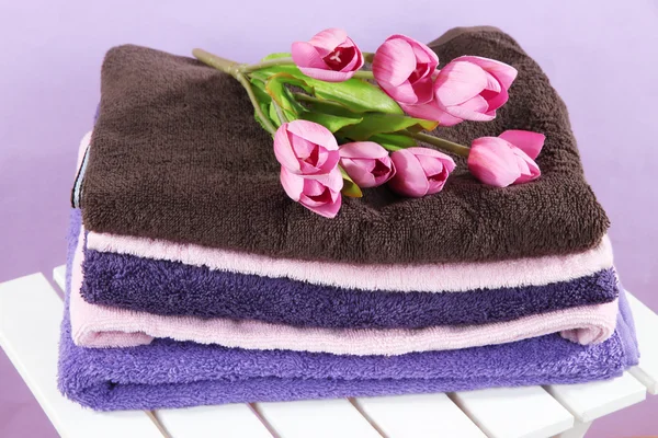 Asciugamani e fiori su sedia di legno su sfondo viola — Foto Stock