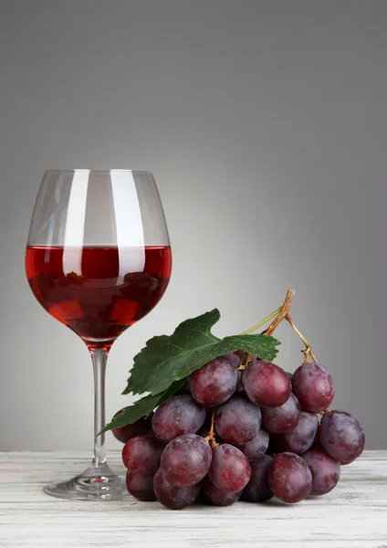 Uvas maduras deliciosas com copo de vinho na mesa em fundo cinza — Fotografia de Stock