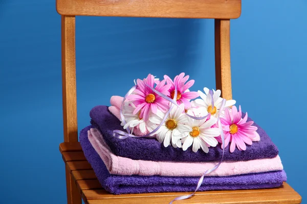 Handtücher und Blumen auf Holzstuhl auf blauem Hintergrund — Stockfoto