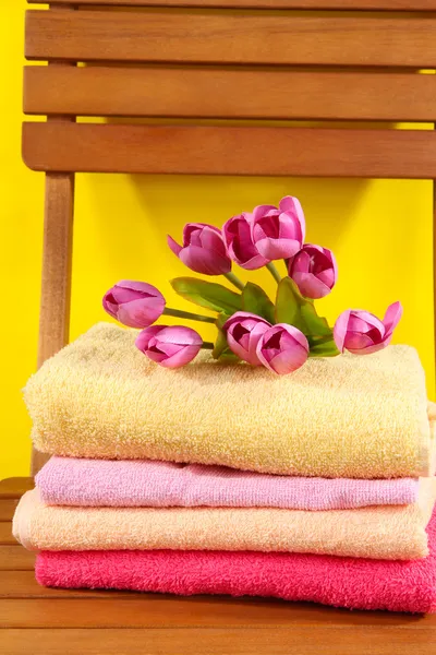 Πετσέτες και λουλούδια σε ξύλινη καρέκλα σε κίτρινο φόντο — Φωτογραφία Αρχείου