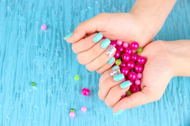 Beautiful woman hands with blue manicure holding pink beads, on color background
