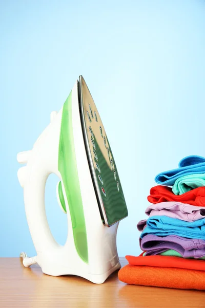 Steam iron with clothes, on color background — Stock Photo, Image